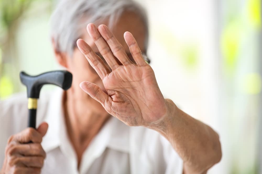 Elderly woman gesturing to stop violence, signaling against mistreatment and abuse of seniors.