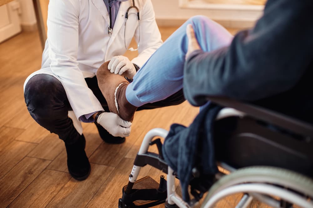 An elderly man in a wheelchair receives a leg examination from a doctor at a nursing home.