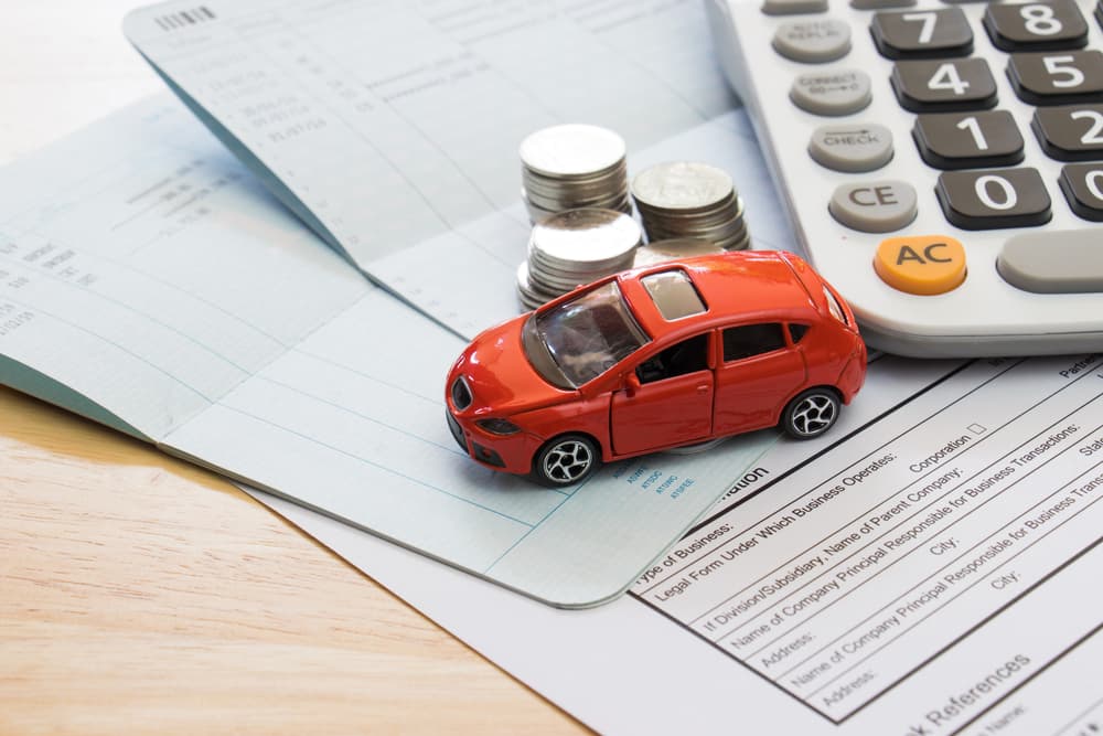 Toy car on financial documents with calculator and coins, representing car insurance or loan.