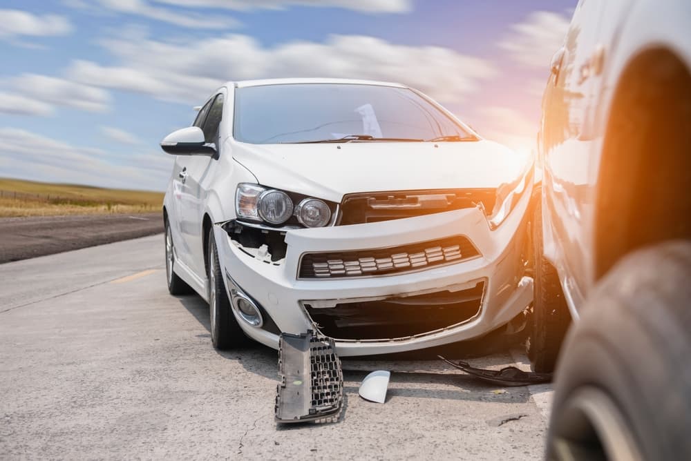 A white car with significant front-end damage after a collision on a sunny day.