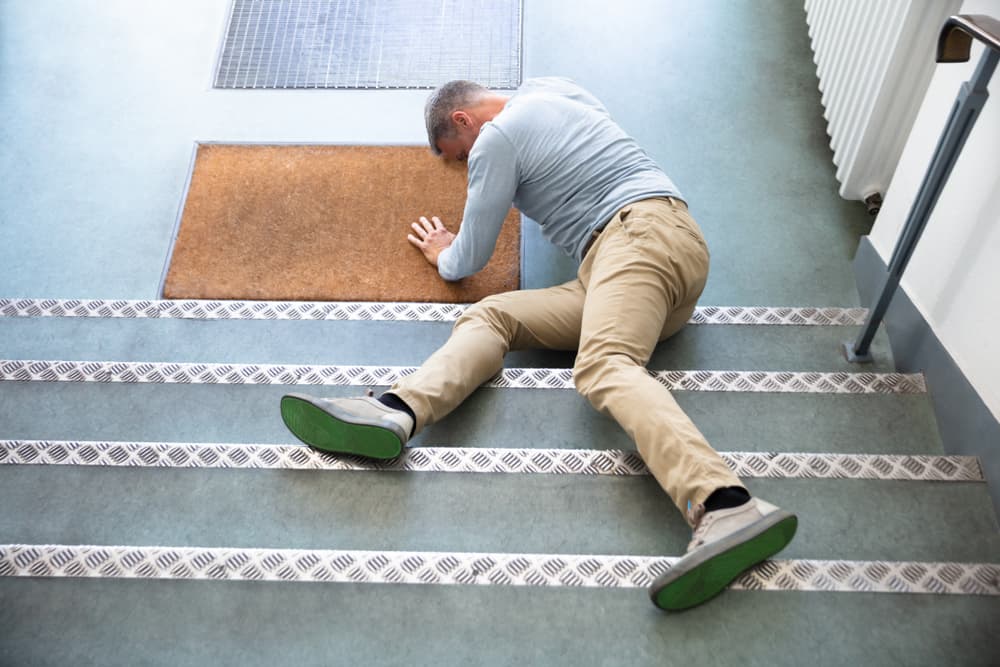 A man lying on stairs after a fall, holding himself up with one arm in distress.