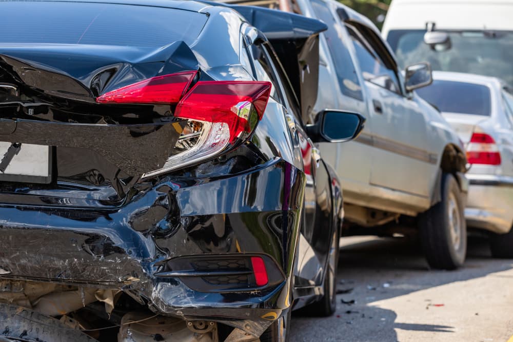 Three cars involved in a rear-end collision, showing significant damage to the back of a black car.