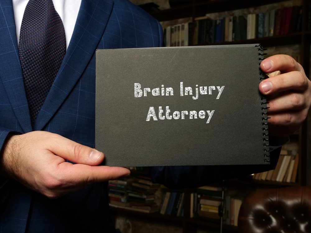 A person in a suit holding a sign that reads "Brain Injury Attorney" in a professional setting.