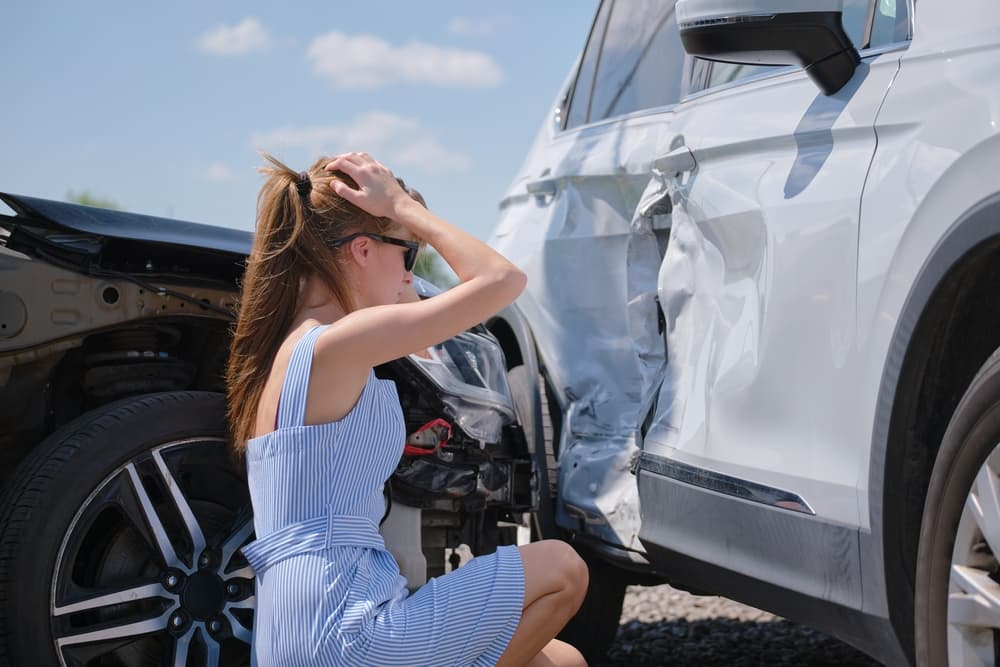 A distressed woman inspecting the damage on the side of a white car after an accident.