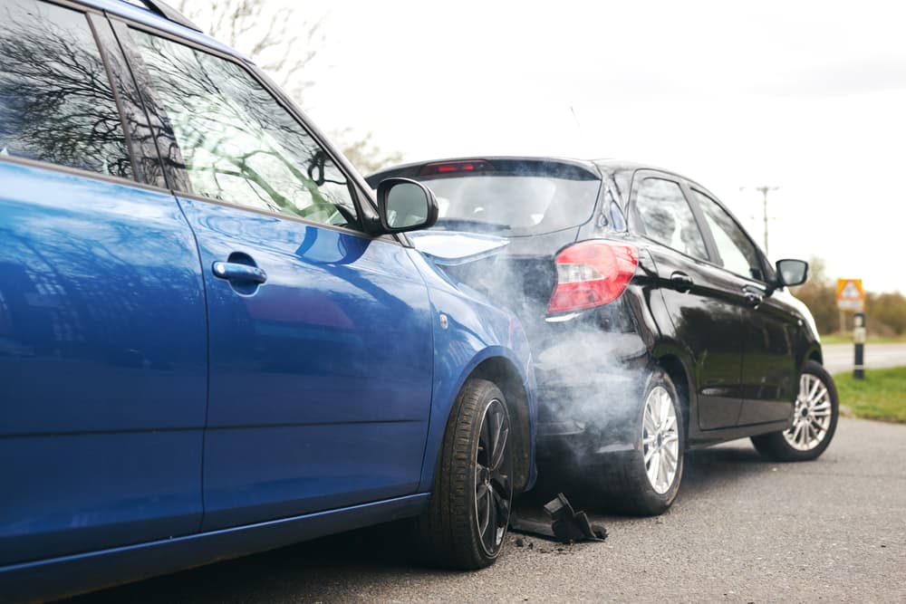 Two cars involved in a rear-end collision on a road, with visible smoke and damage.