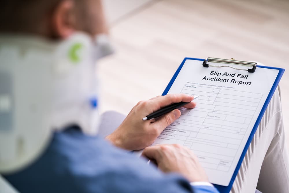 A person wearing a neck brace filling out a "Slip and Fall Accident Report" form on a clipboard.