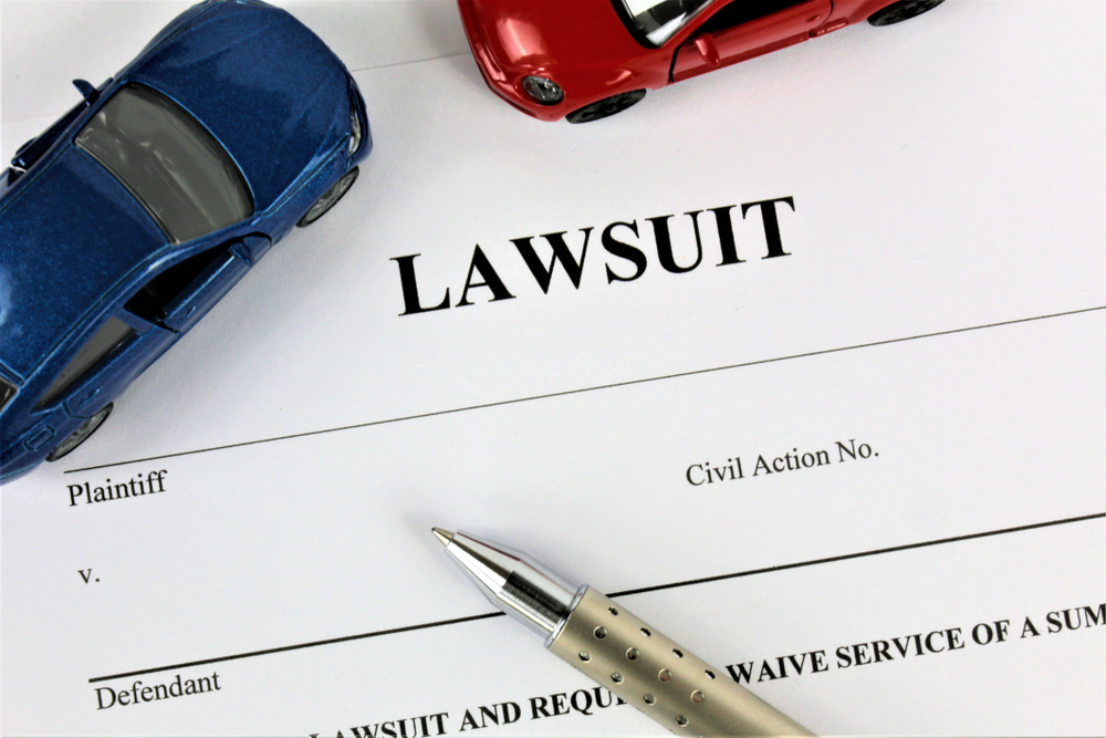 A lawsuit document with a pen and two toy cars, one blue and one red.