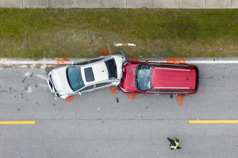 Aerial view of a collision between a white car and a red SUV on a road.