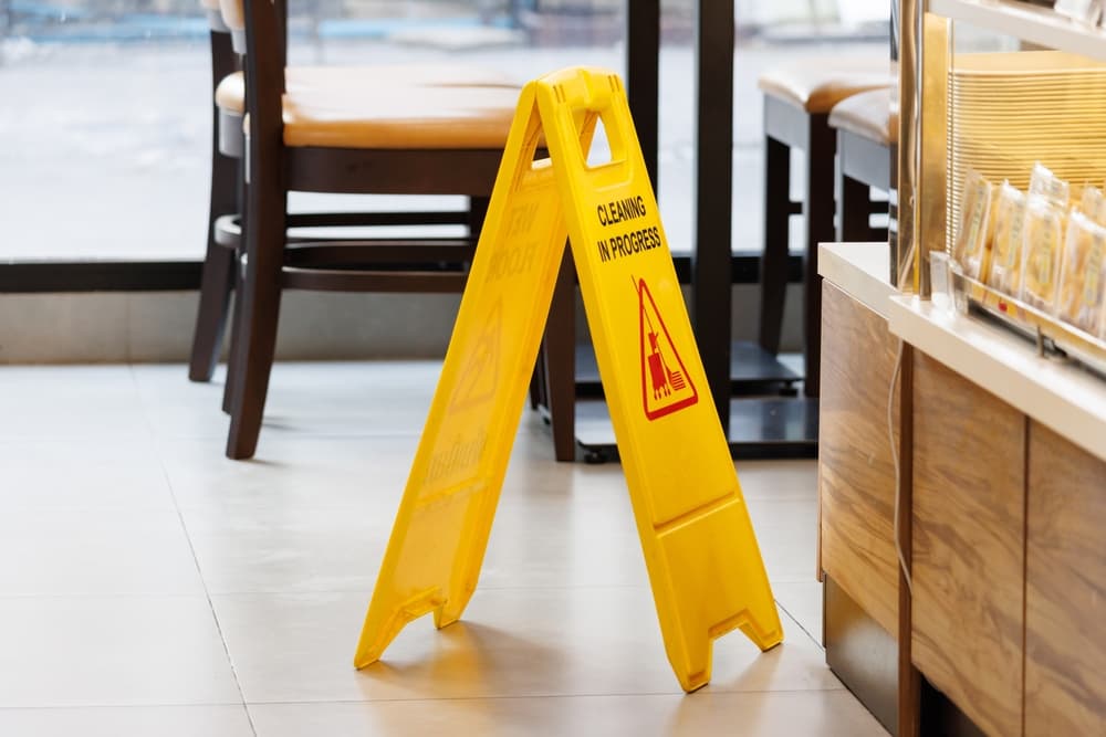 A yellow "Cleaning in Progress" sign placed on the floor of a store near seating area.